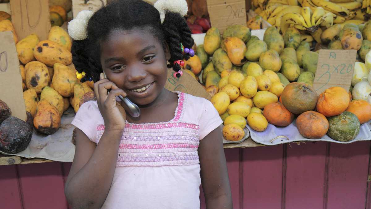 República Dominicana, Santo Domingo, Ciudad, Colonia, Calle Palo Hincado, puesto de frutas, una niña hablando por su teléfono celular. (Foto por: Jeffrey Greenberg/Universal Images Group a través de Getty Images)