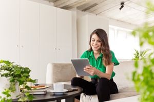 Cheerful young woman wearing green clothes sitting on sofa in the  creative workplace and using digital tablet.