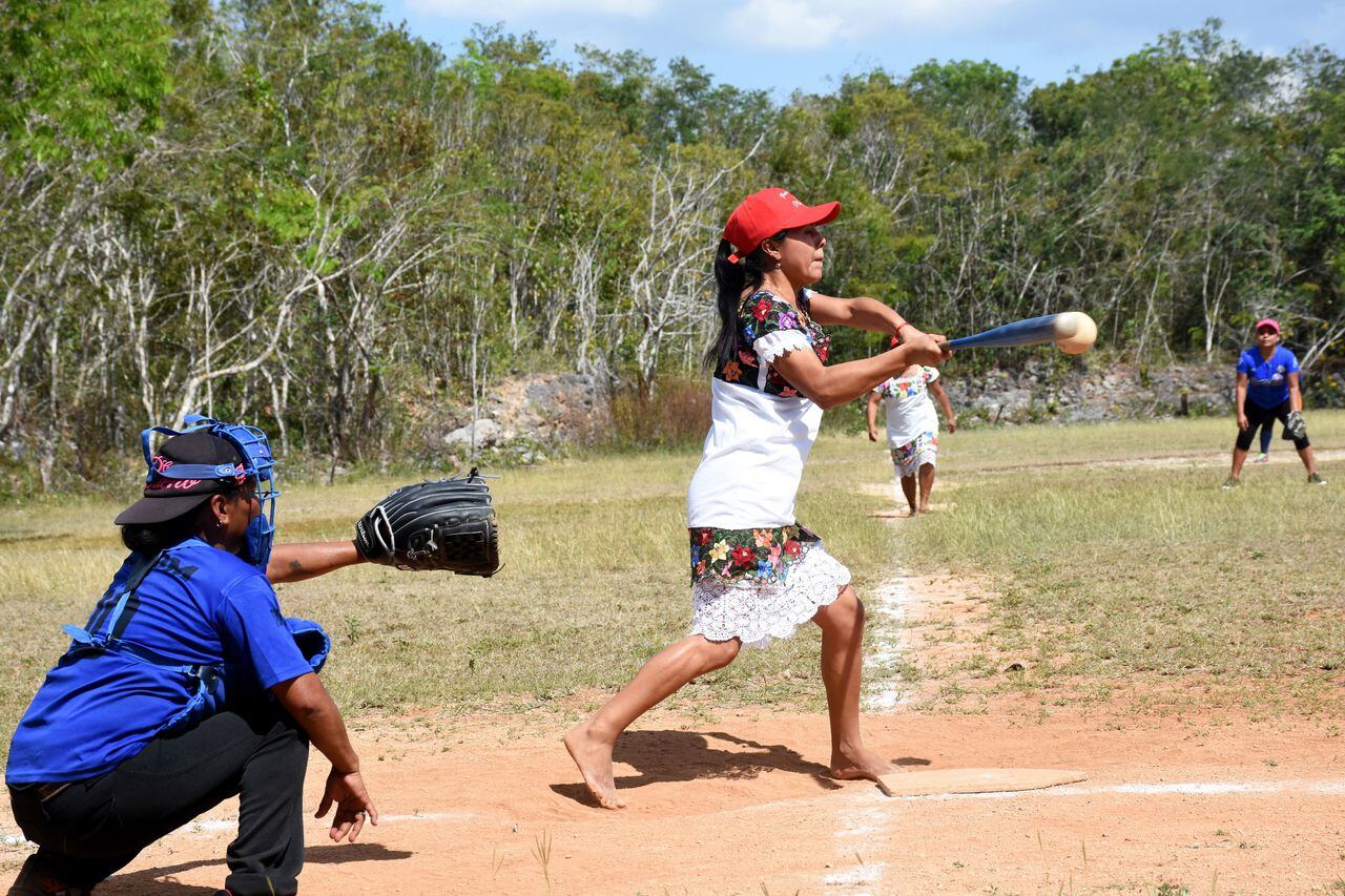 A player of "Las Diablillas de Hondzonot", hits the ball during a softball match against "Guerreras de Piste", in Hondzonot, municipality of Tulum, Quintana Roo State, Mexico, on April 3, 2021. - Barefoot and in finely embroidered white dresses, a group of indigenous women leap onto the diamond. They are Las Diablillas de Hondzonot, a softball team that defies stereotypes in a community in southeastern Mexico. (Photo by ELIZABETH RUIZ / AFP)