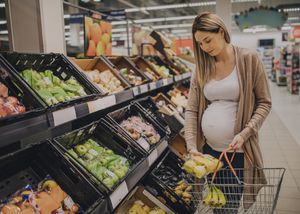 A young pregnant woman is grocery shopping in a supermarket store.