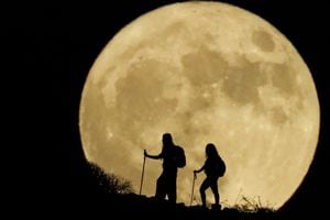 Las mujeres suben una montaña con la luna llena conocida como la "Luna del esturión" de fondo, en Arguineguín, en la isla de Gran Canaria, España, 1 de agosto de 2023. 