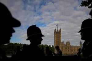 Oficiales de policía hablan cerca de la fila de personas que esperan para presentar sus respetos a la difunta reina Isabel II durante el estado de mentira, en Westminster Hall, Londres, el viernes 16 de septiembre de 2022. (AP Photo/Markus Schreiber)