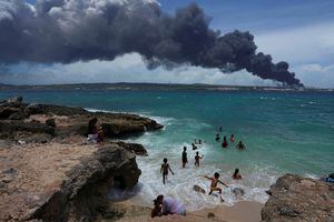 La gente disfruta de la playa cerca del humo de un incendio sobre los tanques de almacenamiento de combustible que explotaron cerca del puerto de superpetroleros de Cuba en Matanzas, Cuba, el 6 de agosto de 2022. Foto REUTERS/Alexandre Meneghini 