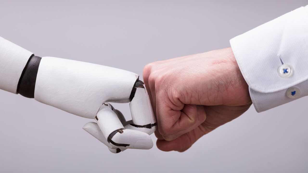 Robot y mano humana haciendo golpe de puño sobre fondo gris - Imagen de referencia