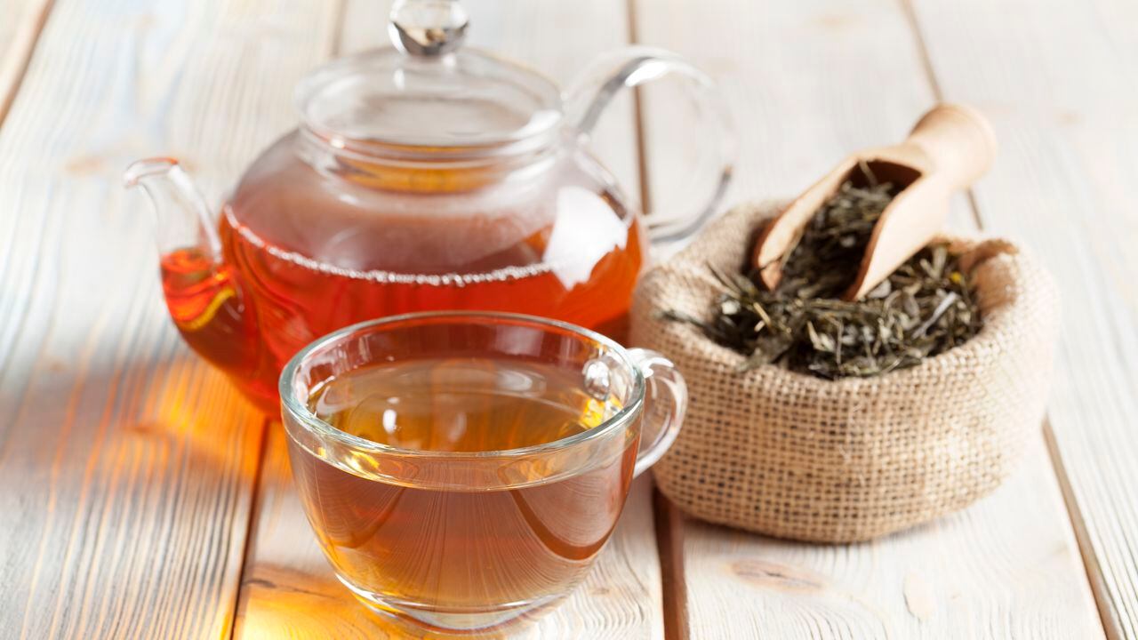 Taza de té, tetera y hojas de té en la mesa de madera