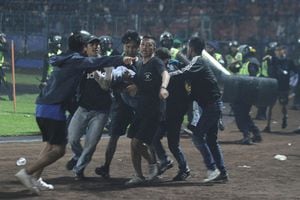 Los partidarios evacuan a un hombre golpeado por gas lacrimógeno disparado por la policía durante los disturbios después del partido de fútbol de la liga BRI Liga 1 entre Arema vs Persebaya en el estadio Kanjuruhan, Malang, provincia de Java Oriental, Indonesia, el 2 de octubre de 2022,