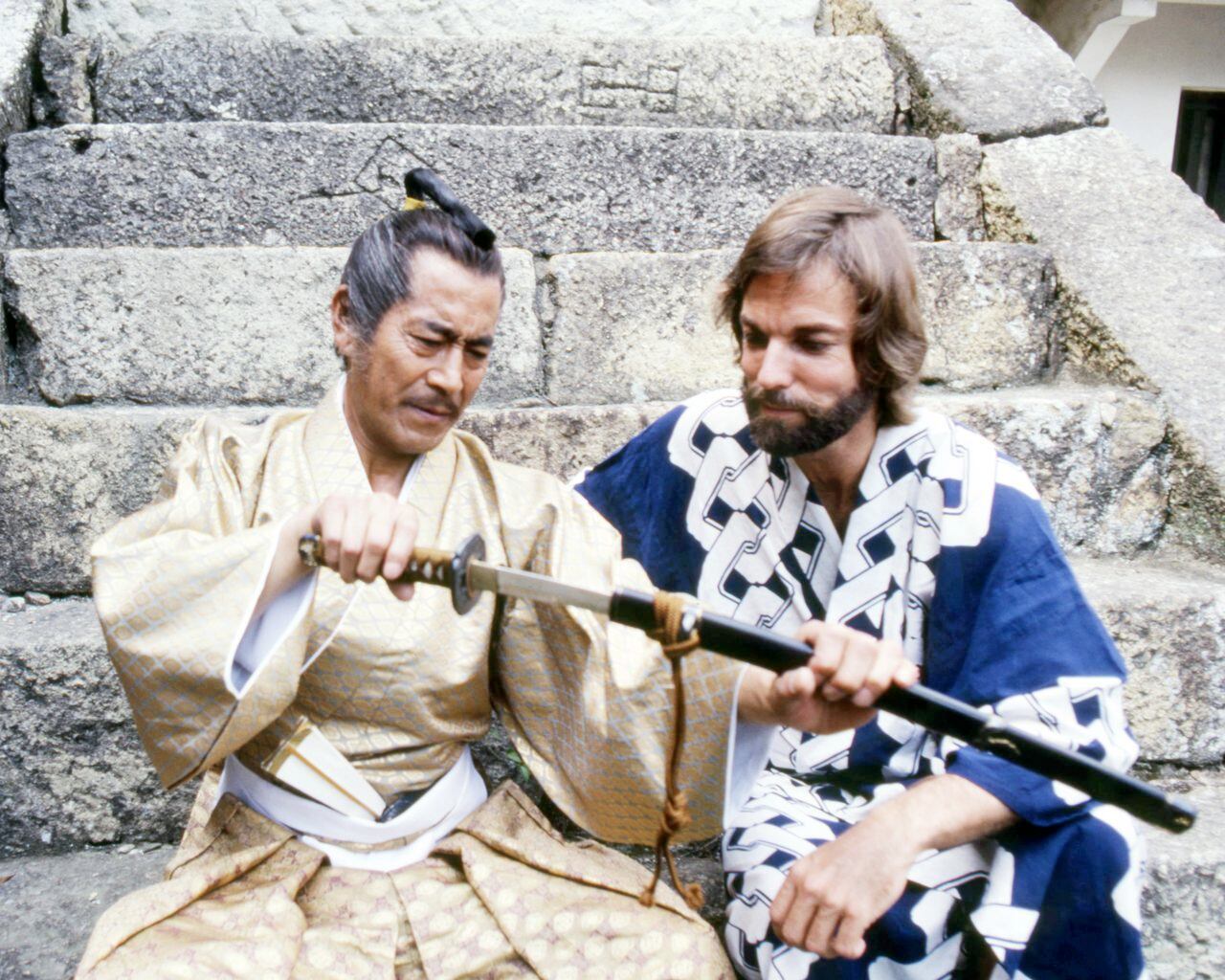Toshiro Mifune (1920 - 1997, left), as Yoshi Toranaga, and American actor Richard Chamberlain as John Blackthorne, examine a samurai sword in the TV miniseries 'Shogun', 1980. (Photo by Silver Screen Collection/Getty Images)