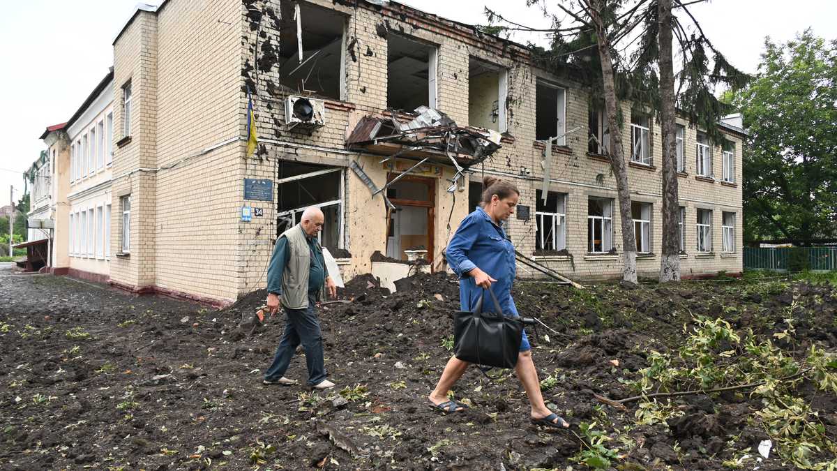 Los residentes locales pasan junto a un edificio dañado parcialmente destruido después de un bombardeo en la ciudad de Chuguiv, al este de Kharkiv, el 16 de julio de 2022. - En la región noreste alrededor de Kharkiv, la segunda ciudad de Ucrania, el gobernador Oleg Synegubov dijo que un ataque nocturno con misiles rusos mató tres personas en el pueblo de Chuguiv. (Foto de SERGEY BOBOK / AFP)