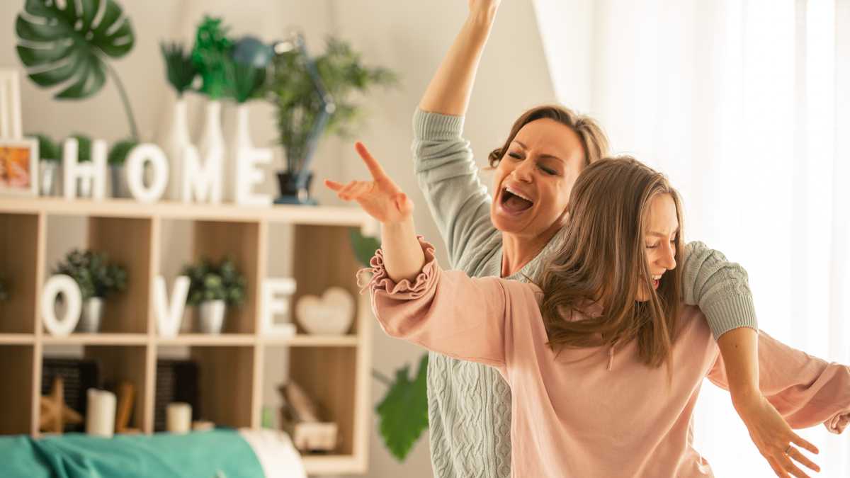 Mother and her daughter captured in the moment of pure joy and laughter while dancing and singing together in their living room.