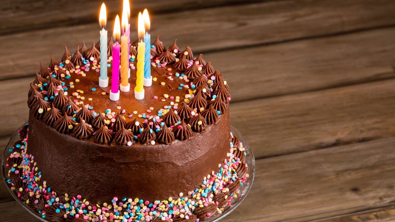 Pastel de cumpleaños de chocolate con chispitas de colores y velas sobre fondo de madera.