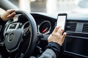Close up of a female hand using phone to search the location while driving a car. Woman using gps navigation on her mobile phone while driving a car.