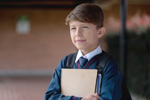 Retrato de un estudiante reflexivo en la escuela vistiendo su uniforme mientras sostiene un cuaderno
