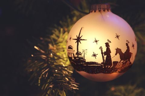 Adorno navideño con silueta de belén con María, José y Belén. El adorno cuelga de la rama del árbol
