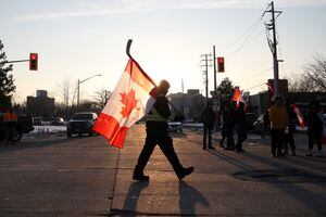 Las personas sostienen banderas canadienses mientras los vehículos bloquean la ruta que va desde el puente Ambassador, que une Detroit y Windsor, mientras los camioneros y sus seguidores continúan protestando contra los mandatos de vacunación contra la enfermedad del coronavirus (COVID-19), en Windsor, Ontario, Canadá. Foto REUTERS/Carlos Osorio