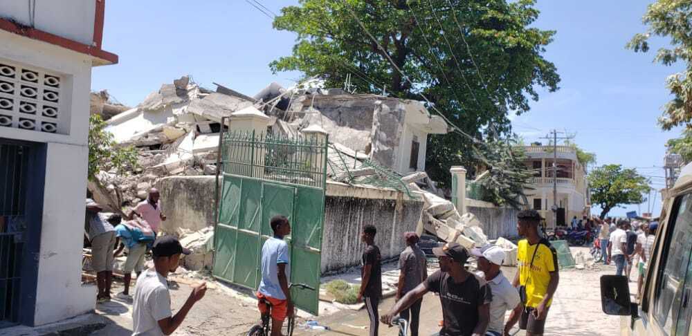 People stand outside the residence of the Catholic bishop after it was damaged by an earthquake in Les Cayes, Haiti, Saturday, Aug. 14, 2021. (AP Photo/Delot Jean)