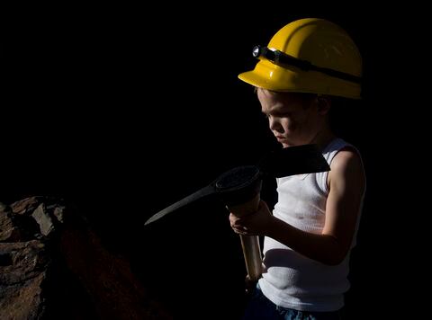 "Young child with hard hat, and pick axe is forced to work mine."