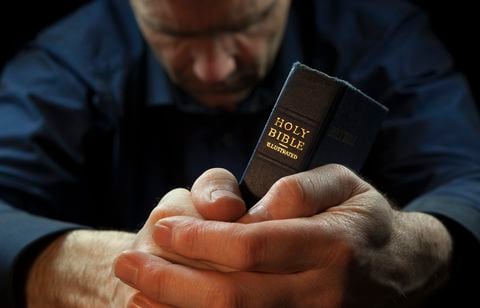 A Man praying holding a Holy Bible