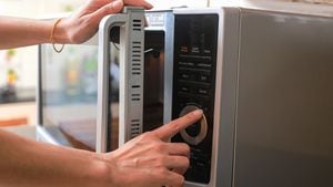 Manos de mujer cerrando la puerta del horno de microondas y preparando comida en el microondas.