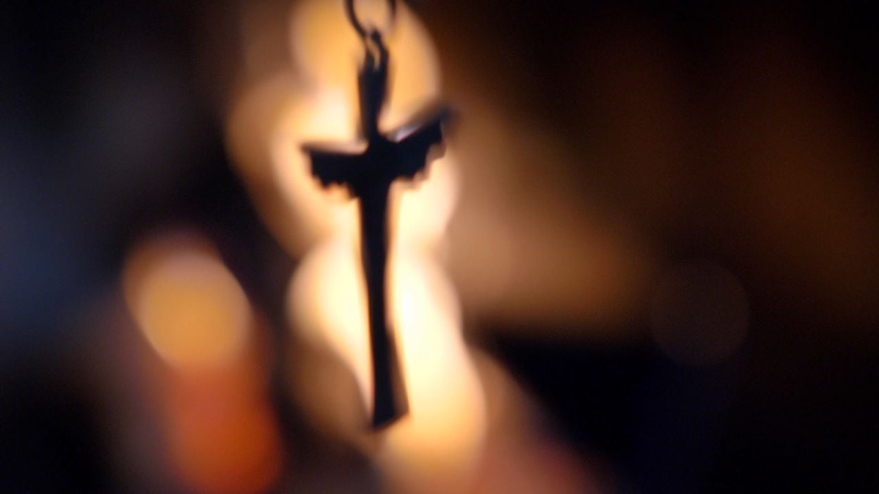 Silueta de crucifijo borrosa sobre llamas de fuego fondo oscuro cámara lenta