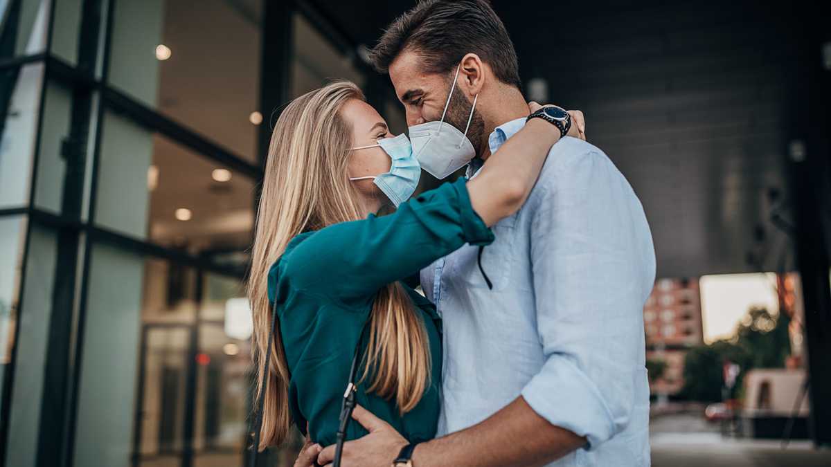Una joven pareja con tapabocas y besándose al aire libre en la ciudad.