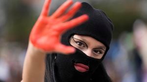 Una mujer enmascarada muestra la palma teñida de rojo de su mano durante la marcha del Día Internacional de la Mujer en Bogotá, Colombia, el miércoles 8 de marzo 2023. (AP Foto/Fernando Vergara)