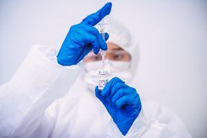 Doctor en guantes protectores y jeringa de inyección de llenado de ropa de trabajo con vacuna COVID-19