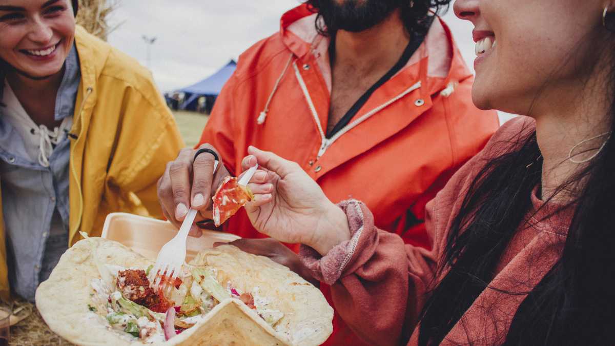 Three friends enjoy sharing some take away  food while at a music festival