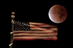 La sombra de la tierra cubre la luna llena durante un eclipse lunar parcial cuando se pone más allá de la bandera de los Estados Unidos en la parte superior de un edificio, el viernes 19 de noviembre de 2021, en el centro de Kansas City, Missouri Foto AP / Charlie Riedel