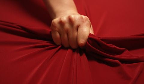Woman hand passionately squeezes red bed sheet. Love concept.
