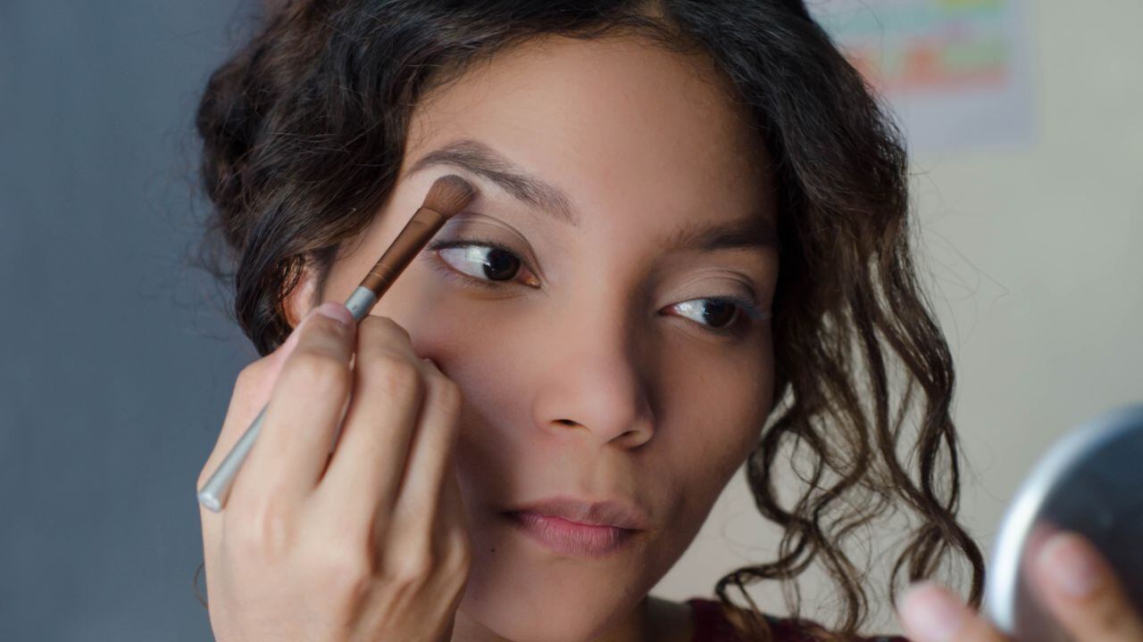 Mujer hermosa joven aplicando sombra de ojos con una brocha de maquillaje en el hueso de la frente