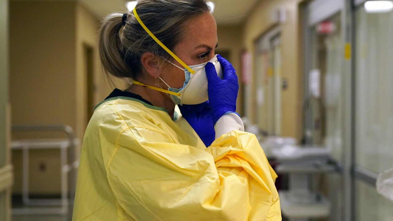 FILE - In this Nov. 24, 2020, file photo, registered nurse Chrissie Burkhiser puts on personal protective equipment as she prepares to treat a COVID-19 patient in the emergency room at Scotland County Hospital in Memphis, Mo. U.S. hospitals slammed with COVID-19 patients are trying to lure nurses and doctors out of retirement and recruiting nursing students and new graduates who have yet to earn their licenses. (AP Photo/Jeff Roberson, File)
