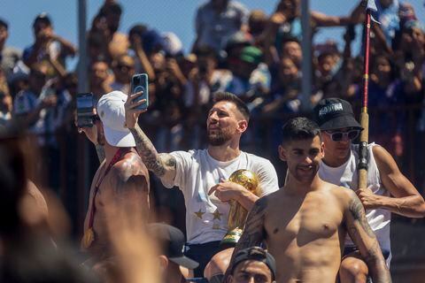 Argentine football star Lionel Messi (C) takes pictures with his phone while celebrating on board a bus with a sign reading "World Champions" with supporters after winning the Qatar 2022 World Cup tournament as they tour through Buenos Aires' downtown on December 20, 2022. - Millions of ecstatic fans are expected to cheer on their heroes as Argentina's World Cup winners led by captain Lionel Messi began their open-top bus parade of the capital Buenos Aires on Tuesday following their sensational victory over France. (Photo by TOMAS CUESTA / AFP)