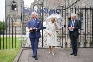 FILE - Britain's King Charles III, left, and Queen Camilla, center, accompanied by the moderator of the High Constables, Roderick Urquhart, right, unveil a plaque at the new Jubilee Gates, installed at the entrance to Abbey Yard to mark the Platinum Jubilee of Queen Elizabeth II, at the Palace of Holyroodhouse, in Edinburgh, Scotland, Tuesday July 4, 2023. A year after the death of Queen Elizabeth II triggered questions about the future of the British monarchy, King Charles III’s reign has been marked more by continuity than transformation, by changes in style rather than substance. (Jonathan Brady/Pool via AP, File)