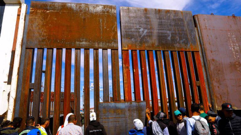 Migrantes esperan cerca del muro fronterizo en el puente internacional Paso del Norte para solicitar asilo en Estados Unidos.