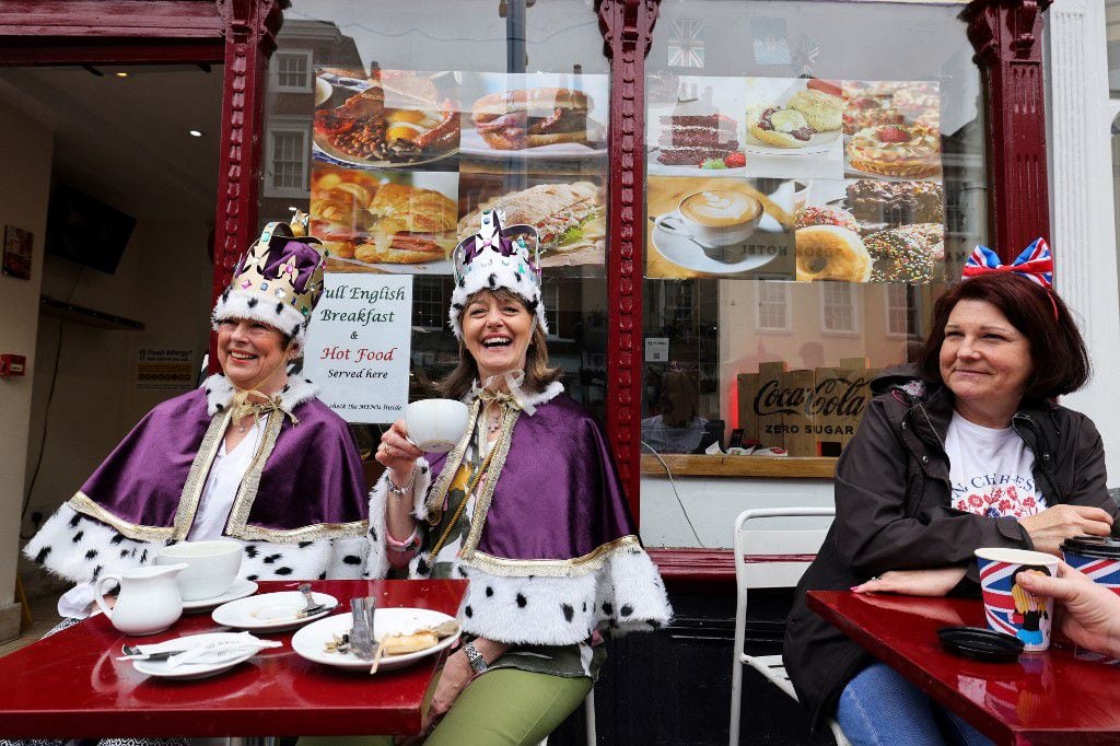 Dos mujeres con coronas toman una taza de té en la calle principal de Windsor antes de un Gran Almuerzo de Coronación organizado en Windsor, el 7 de mayo de 2023.