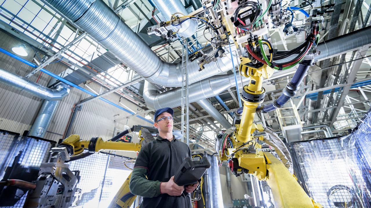 Aprendiz de ingeniero ajustando robot en fábrica de automóviles - Imagen de referencia