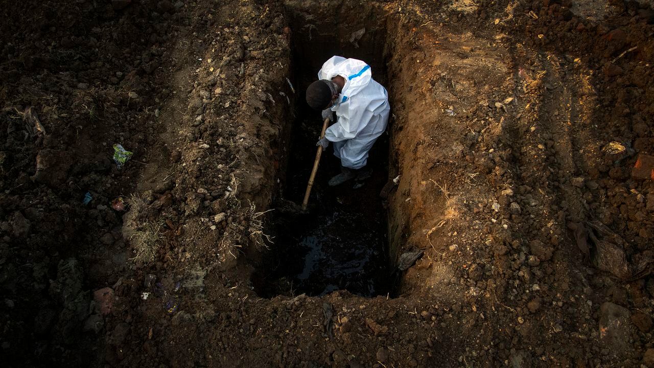Un hombre con un traje de protección cava la tierra para enterrar el cuerpo de una persona que murió a causa de covid-19 en Gauhati, India