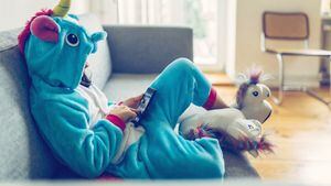 niñita disfrazada de unicornio relajándose con el móvil en el sofá de casa