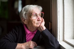Anciana con gafas mirando pensativamente por la ventana.