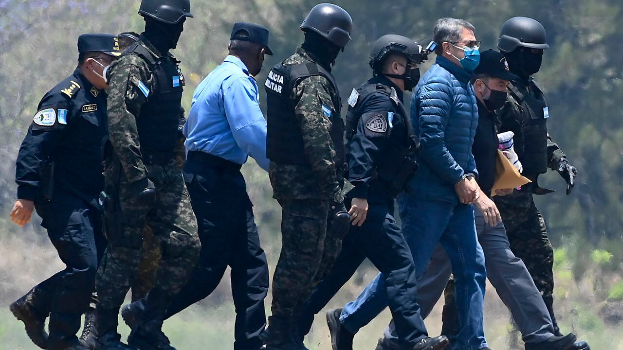El expresidente de Honduras Juan Orlando Hernández (3-R) fue escoltado por agentes policiales a su llegada a una base de la Fuerza Aérea en Tegucigalpa, el 21 de abril de 2022, antes de ser extraditado a Estados Unidos para enfrentar cargos relacionados con el narcotráfico. (Foto por Orlando SIERRA / AFP)