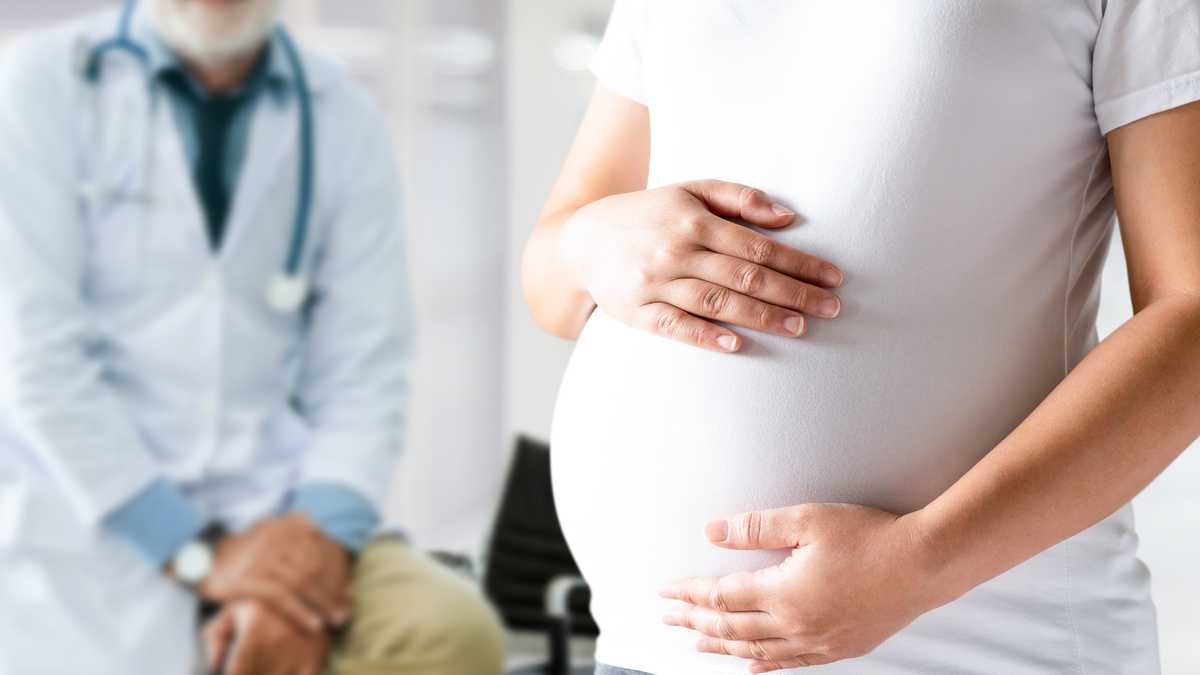 Happy pregnant woman visiting gynecologist doctor in hospital or medical clinic for pregnancy consultant.  Doctor examine pregnant woman belly for baby and mother health care check.  Gynecology concept.