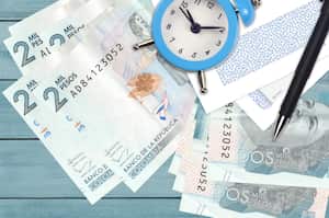 2 Colombian pesos bills and alarm clock with pen and envelopes. Tax season concept, payment deadline for credit or loan. Financial operations using postal service. Quick money transfer