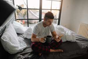Portrait of a man in his bedroom drinking first morning coffee and reading online morning news