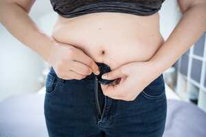 Mujer con sobrepeso que lucha por subirse los pantalones