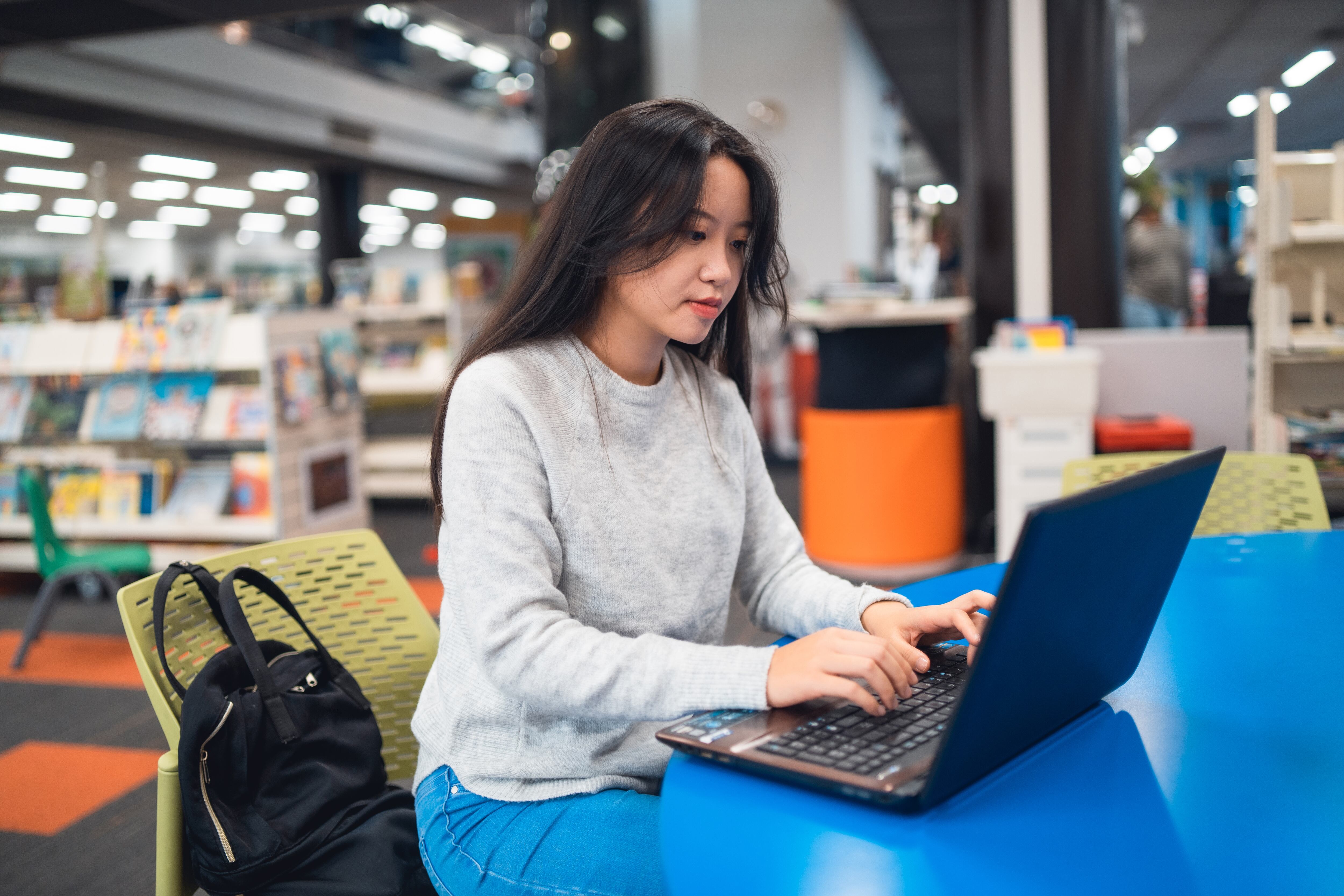Mujer joven trabajando en una computadora portátil en la biblioteca.
