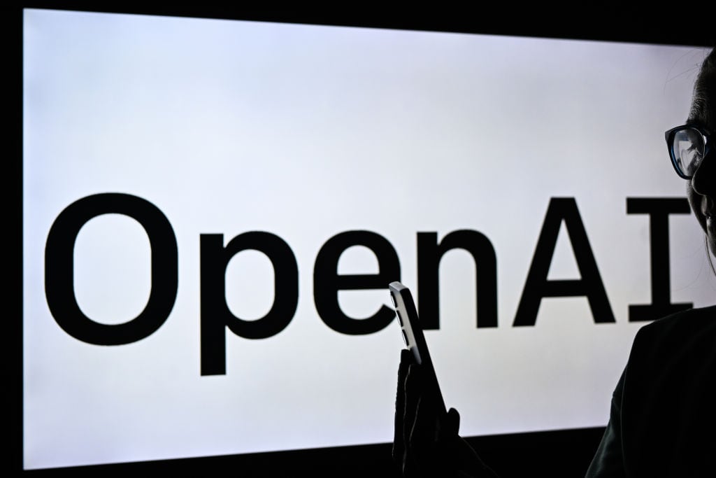 Una mujer sostiene un teléfono celular frente a una pantalla de computadora que muestra el logotipo de OpenAI, el 10 de febrero de 2025, en Edmonton, Canadá. (Foto de Artur Widak/NurPhoto vía Getty Images)