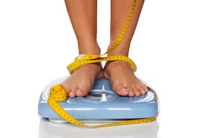 Pies de mujer en una báscula doméstica y cinta métrica alrededor de ellos.