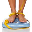 Pies de mujer en una báscula doméstica y cinta métrica alrededor de ellos.