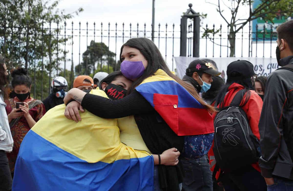 Dos manifestantes que usan tapabocas se abrazan en medio de la protesta mientras portan banderas de Colombia para protestar en contra de las masacres y la violencia de los últimos días. Foto Guillermo Torres / Semana