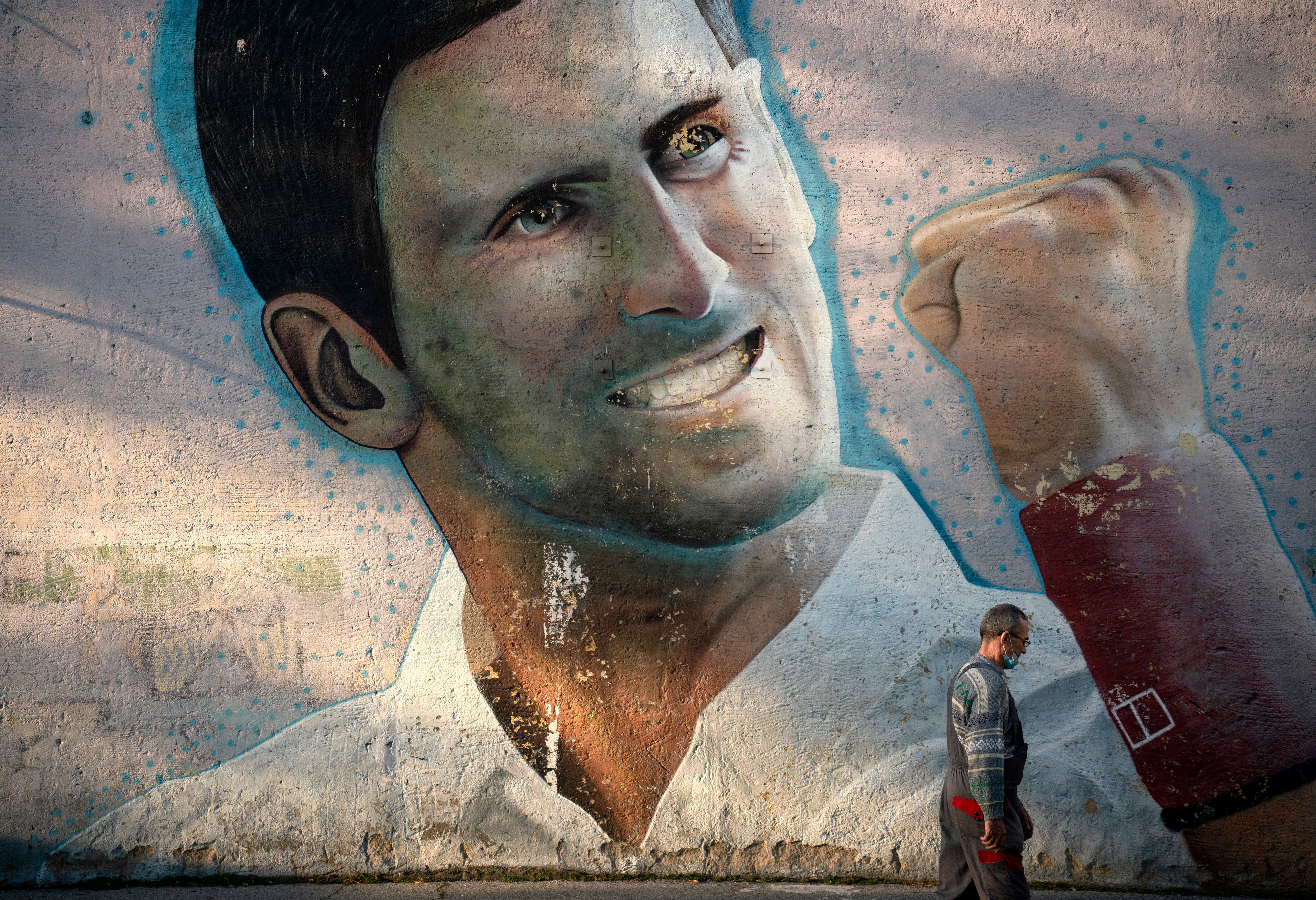 Un hombre pasa junto a un mural que representa al tenista serbio Novak Djokovic, pintado en la pared exterior de una escuela primaria, en Belgrado el 14 de enero de 2022. - Australia canceló la visa de Novak Djokovic por segunda vez el 14 de enero de 2022, en un sensacional nuevo intento de deportar a la superestrella del tenis Covid-19 no vacunada. El gobierno conservador del país, derrotado una vez en los tribunales, invocó poderes ejecutivos extraordinarios para desmantelar nuevamente la visa del serbio de 34 años por motivos de interés público. El movimiento se produjo solo tres días antes de que comience el Abierto de Australia, poniendo en seria duda el sueño de Djokovic de un récord de 21 Grand Slam. (Foto de OLIVER BUNIC / AFP)
